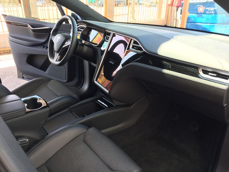 The cream and black interior of a Tesla, dashboard and front seats, seen through the open door.