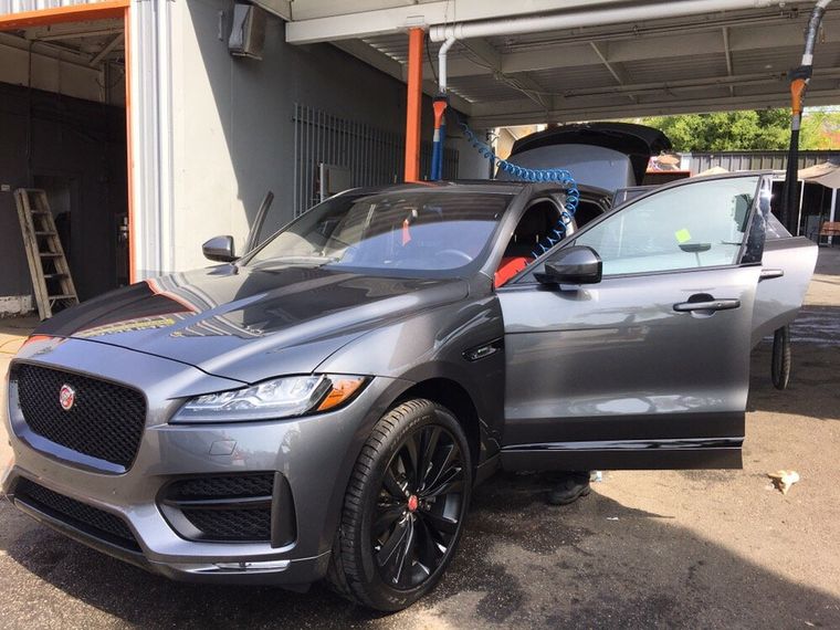 A silver Jaguar SUV with its doors open in the wash bay beside orange steel columns.