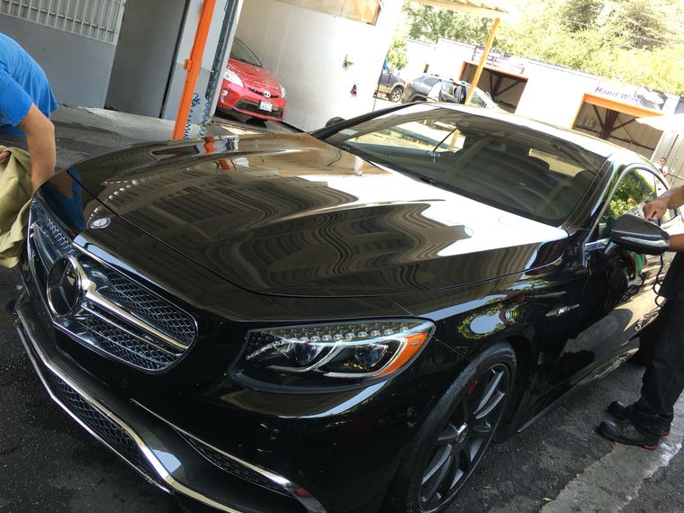 A black Mercedes coupe with the sky reflected in its hood, parked under the canopy.