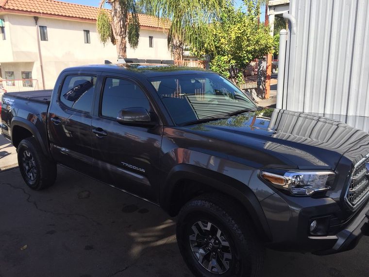 A grey Toyota Tacoma pickup parked on the lot with palm trees behind it.